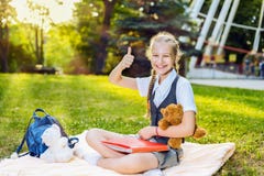 Большой палец руки студента школьницы счастливый усмехаясь показывая вверх сидит на одеяле в парке на солнечный день подросток де стоковые фотографии rf Большой палец руки студента школьницы счастливый усмехаясь показывая вверх сидит на одеяле в парке на солнечный день подросток де стоковые фотографии rf