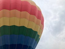 Большой пестротканой яркой круглой воздушный шар летая покрашенный радугой striped striped с корзиной против неба в вечере стоковое фото rf Большой пестротканой яркой круглой воздушный шар летая покрашенный радугой striped striped с корзиной против неба в вечере стоковое фото rf