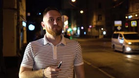 Бородатый человек в iqos сигареты striped дыма поло электронных вечером на улице с автомобилями на предпосылке и идти вниз сток-видео Бородатый человек в iqos сигареты striped дыма поло электронных вечером на улице с автомобилями на предпосылке и идти вниз сток-видео