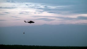 Вертолет огня груза с приостанавливанным ковшом водосброса летает от резервуара Вертолет огня груза с приостанавливанным ковшом водосброса летает от резервуара
