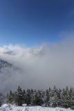 Верхняя часть гор при лес покрытый с снегом, туманом и облаками на солнечный морозный день стоковые изображения rf Верхняя часть гор при лес покрытый с снегом, туманом и облаками на солнечный морозный день стоковые изображения rf
