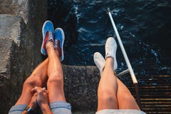 Взгляд верхней части близкий поднимающий вверх молодых ног пар в тапках сидя на пристани близко к морю, концепции перемещения стоковые фотографии rf Взгляд верхней части близкий поднимающий вверх молодых ног пар в тапках сидя на пристани близко к морю, концепции перемещения стоковые фотографии rf