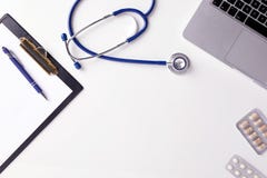 Взгляд сверху стола доктора со стетоскопом, latptop, таблетками и чистым листом бумаги на доске сзажимом для бумаги с космосом эк стоковое изображение rf Взгляд сверху стола доктора со стетоскопом, latptop, таблетками и чистым листом бумаги на доске сзажимом для бумаги с космосом эк стоковое изображение rf
