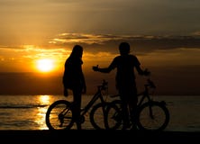 Взгляд со стороны пар стоя на seashore с их велосипедами и наслаждаясь заходом солнца стоковые фото Взгляд со стороны пар стоя на seashore с их велосипедами и наслаждаясь заходом солнца стоковые фото