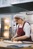 Взрослая женщина в стеклах и рисберме печет торты в хлебопекарне стоковые фотографии rf Взрослая женщина в стеклах и рисберме печет торты в хлебопекарне стоковые фотографии rf
