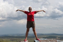 Взрослая женщина стоит, оружия протягиванные, на высокой горе, против фона равнины и облачного неба стоковые изображения rf Взрослая женщина стоит, оружия протягиванные, на высокой горе, против фона равнины и облачного неба стоковые изображения rf