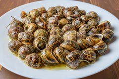 Вкусные зажаренные улитки в белом блюде на коричневой деревянной предпосылке Стоковая Фотография RF Вкусные зажаренные улитки в белом блюде на коричневой деревянной предпосылке Стоковая Фотография RF