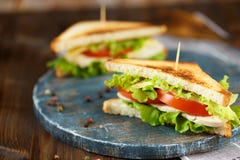 Вкусный сэндвич 2 с цыпленком, томатами, салатом, сыром на деревянной плите на темной предпосылке стоковые фотографии rf Вкусный сэндвич 2 с цыпленком, томатами, салатом, сыром на деревянной плите на темной предпосылке стоковые фотографии rf