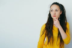 Внимательная сомнительная красивая девушка с dreadlocks и в желтом ярком свитере с неуверенной рукой удерживания стороны на подбо стоковое фото rf Внимательная сомнительная красивая девушка с dreadlocks и в желтом ярком свитере с неуверенной рукой удерживания стороны на подбо стоковое фото rf