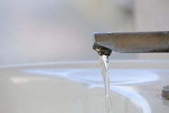 Вода пропуская от старого стального faucet с нерезкостью белая предпосылка раковины в уборной стоковое фото rf Вода пропуская от старого стального faucet с нерезкостью белая предпосылка раковины в уборной стоковое фото rf