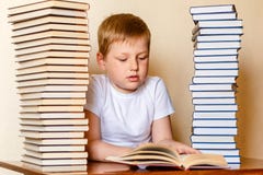 Восьмилетний кавказский мальчик в белой футболке читая книгу, сидя на таблице стоковое изображение rf Восьмилетний кавказский мальчик в белой футболке читая книгу, сидя на таблице стоковое изображение rf