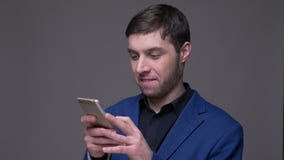 Всход крупного плана молодого красивого кавказского человека используя телефон смотря камеру и усмехаясь с предпосылкой изолирова акции видеоматериалы Всход крупного плана молодого красивого кавказского человека используя телефон смотря камеру и усмехаясь с предпосылкой изолирова акции видеоматериалы