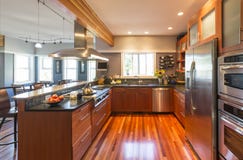 Высококачественная современная домашняя кухня с деревянными шкафами, паркетом, приборами нержавеющей стали, окнами и освещением а стоковые изображения rf Высококачественная современная домашняя кухня с деревянными шкафами, паркетом, приборами нержавеющей стали, окнами и освещением а стоковые изображения rf