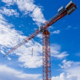 Высокорослый кран башни над строительной площадкой с голубым небом и облаками позади стоковые фотографии rf Высокорослый кран башни над строительной площадкой с голубым небом и облаками позади стоковые фотографии rf