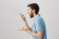 Глупый телефон Студия сняла сердитого шального бородатого парня крича на smartphone пока говорящ на дикторе или был сумашедшим ус стоковые фотографии rf Глупый телефон Студия сняла сердитого шального бородатого парня крича на smartphone пока говорящ на дикторе или был сумашедшим ус стоковые фотографии rf