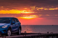 Голубой компактный автомобиль SUV со спортом и современным дизайном припаркованный на конкретной дороге морским путем на заходе с стоковая фотография Голубой компактный автомобиль SUV со спортом и современным дизайном припаркованный на конкретной дороге морским путем на заходе с стоковая фотография