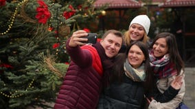 Группа в составе усмехаясь человек и женщины принимая Selfie Outdoors около дерева Xmas Друзья имея потеху на рождественской ярма сток-видео Группа в составе усмехаясь человек и женщины принимая Selfie Outdoors около дерева Xmas Друзья имея потеху на рождественской ярма сток-видео