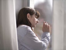 Грустная молодая женщина брюнета смотрит вне окно с ее рукой на стекле стоковая фотография rf Грустная молодая женщина брюнета смотрит вне окно с ее рукой на стекле стоковая фотография rf
