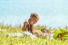 Девушка в купальном костюме сидит сиротливое на пляже на траве около реки на солнечный день Девушка грустна на стоковое изображение Девушка в купальном костюме сидит сиротливое на пляже на траве около реки на солнечный день Девушка грустна на стоковое изображение