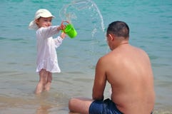 Девушка льет воду на ее отце Брызгает воды в море Ребенок и отец на каникулах стоковое изображение Девушка льет воду на ее отце Брызгает воды в море Ребенок и отец на каникулах стоковое изображение
