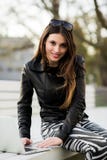 Девушка работает при портативный компьютер сидя на стенде в парке смотря к камере и усмехаться Стоковое Изображение RF Девушка работает при портативный компьютер сидя на стенде в парке смотря к камере и усмехаться Стоковое Изображение RF