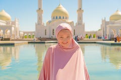 Девушка ребенк в розовом hijab сидит рядом с белой мечетью и улыбками r стоковое фото rf Девушка ребенк в розовом hijab сидит рядом с белой мечетью и улыбками r стоковое фото rf