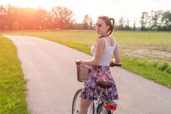 Девушка с велосипедом на заходе солнца лета на дороге в парке города Колесо крупного плана цикла на запачканной предпосылке лета стоковое изображение Девушка с велосипедом на заходе солнца лета на дороге в парке города Колесо крупного плана цикла на запачканной предпосылке лета стоковое изображение