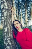 Девушка с красными губами в красном стиле моды платья стоит в роще березы стоковые изображения rf Девушка с красными губами в красном стиле моды платья стоит в роще березы стоковые изображения rf