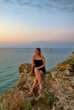 Девушка сидит на утесе и смотрит красивый вид моря и захода солнца стоковое фото rf Девушка сидит на утесе и смотрит красивый вид моря и захода солнца стоковое фото rf