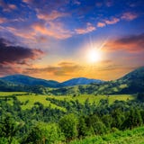 Деревня на луге горного склона с лесом в горе на заходе солнца стоковое фото rf Деревня на луге горного склона с лесом в горе на заходе солнца стоковое фото rf