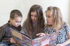 3 дет имея потеху читая книгу 2 сестры и брат Светлая предпосылка Европейское возникновение стоковые фотографии rf 3 дет имея потеху читая книгу 2 сестры и брат Светлая предпосылка Европейское возникновение стоковые фотографии rf