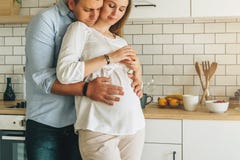 Детеныши поженились объятия пар стоя близко таблица в кухне его обнимает супруги супруга супоросого Образ жизни, счастливые люди стоковое изображение rf Детеныши поженились объятия пар стоя близко таблица в кухне его обнимает супруги супруга супоросого Образ жизни, счастливые люди стоковое изображение rf