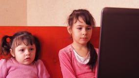 Дети играя в компьтер-книжке 2 маленькой девочки напечатаны на компьтер-книжке 2 сестры сидя на оранжевом кресле смотря подол видеоматериал Дети играя в компьтер-книжке 2 маленькой девочки напечатаны на компьтер-книжке 2 сестры сидя на оранжевом кресле смотря подол видеоматериал