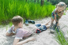 Дети отпрыска играя на дюне пляжа и хороня один другого в белом песке на предпосылке сосновой древесины стоковая фотография rf Дети отпрыска играя на дюне пляжа и хороня один другого в белом песке на предпосылке сосновой древесины стоковая фотография rf