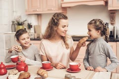 Дети с матерью в кухне Семья выпивает чай с круассанами стоковое фото Дети с матерью в кухне Семья выпивает чай с круассанами стоковое фото