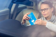 Довольно, молодая женщина управляя ее новое автомобильным кладущ необходимые паркуя часы за лобовым стеклом стоковая фотография rf Довольно, молодая женщина управляя ее новое автомобильным кладущ необходимые паркуя часы за лобовым стеклом стоковая фотография rf