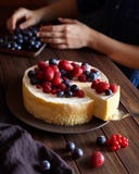 Домодельный сметанообразный чизкейк Нью-Йорка mascarpone с ягодами на темном деревянном столе Руки в рамке стоковые изображения Домодельный сметанообразный чизкейк Нью-Йорка mascarpone с ягодами на темном деревянном столе Руки в рамке стоковые изображения