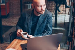 Думая привлекательный взрослый успешный лысый бородатый человек в костюме с ноутбуком в кафе стоковая фотография rf Думая привлекательный взрослый успешный лысый бородатый человек в костюме с ноутбуком в кафе стоковая фотография rf