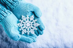 Женские руки в светлом teal связали mittens с сверкная чудесной снежинкой на белой предпосылке снега Концепция рождества зимы Женские руки в светлом teal связали mittens с сверкная чудесной снежинкой на белой предпосылке снега Концепция рождества зимы