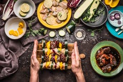Женские руки держа различные домодельные протыкальники овощей мяса для гриля или bbq на деревенской предпосылке с ингридиентами, стоковое фото rf Женские руки держа различные домодельные протыкальники овощей мяса для гриля или bbq на деревенской предпосылке с ингридиентами, стоковое фото rf