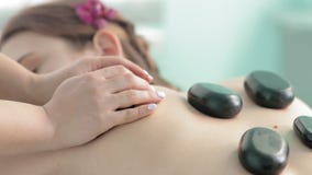 Женский masseur обрабатывает заднюю часть женщин с горячим каменным замедленным движением терапией сток-видео Женский masseur обрабатывает заднюю часть женщин с горячим каменным замедленным движением терапией сток-видео