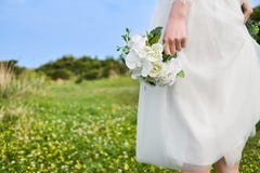 Женщина в белизне зашнуровала bridal платье держа белый букет на ее стороне на желтом поле цветения устроенном на скале стоковое изображение rf Женщина в белизне зашнуровала bridal платье держа белый букет на ее стороне на желтом поле цветения устроенном на скале стоковое изображение rf