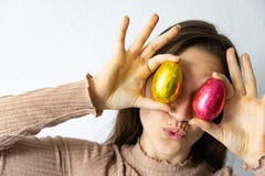 Женщина держа красные и золотые пасхальные яйца шоколада перед ее глазами стоковые фотографии rf Женщина держа красные и золотые пасхальные яйца шоколада перед ее глазами стоковые фотографии rf