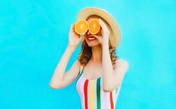 Женщина портрета лета счастливая усмехаясь держа в ее руках 2 куска оранжевого плода пряча ее глаза в соломенной шляпе на красочн стоковое изображение rf Женщина портрета лета счастливая усмехаясь держа в ее руках 2 куска оранжевого плода пряча ее глаза в соломенной шляпе на красочн стоковое изображение rf