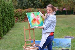 Женщина художника держит картину и смотрит ее, представляющ на камере стоковое изображение Женщина художника держит картину и смотрит ее, представляющ на камере стоковое изображение