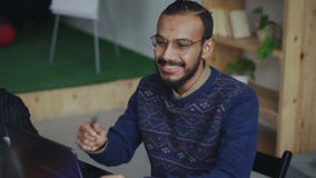 Жизнерадостный Афро-американский человек в стеклах усмехаясь пока обсуждающ о новом start-up проекте с командой в офисе сток-видео Жизнерадостный Афро-американский человек в стеклах усмехаясь пока обсуждающ о новом start-up проекте с командой в офисе сток-видео