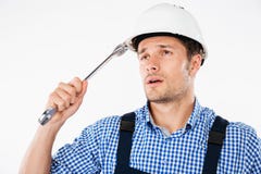 Задумчивый красивый молодой построитель думая и смотря вверх держащ ключ Стоковые Изображения RF Задумчивый красивый молодой построитель думая и смотря вверх держащ ключ Стоковые Изображения RF