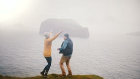 Задний взгляд молодых счастливых пар стоит на береге моря и скакать утехи, обнимая в Исландии сток-видео Задний взгляд молодых счастливых пар стоит на береге моря и скакать утехи, обнимая в Исландии сток-видео