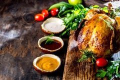 Зажаренный в духовке цыпленк цыпленок с розмариновым маслом служил на черной плите с соусами на деревянном столе, взгляд сверху стоковое изображение Зажаренный в духовке цыпленк цыпленок с розмариновым маслом служил на черной плите с соусами на деревянном столе, взгляд сверху стоковое изображение
