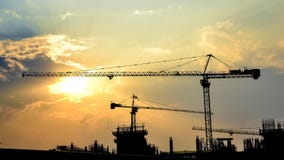 Заход солнца промежутка времени и кран силуэта в строительной площадке Заход солнца промежутка времени и кран силуэта в строительной площадке
